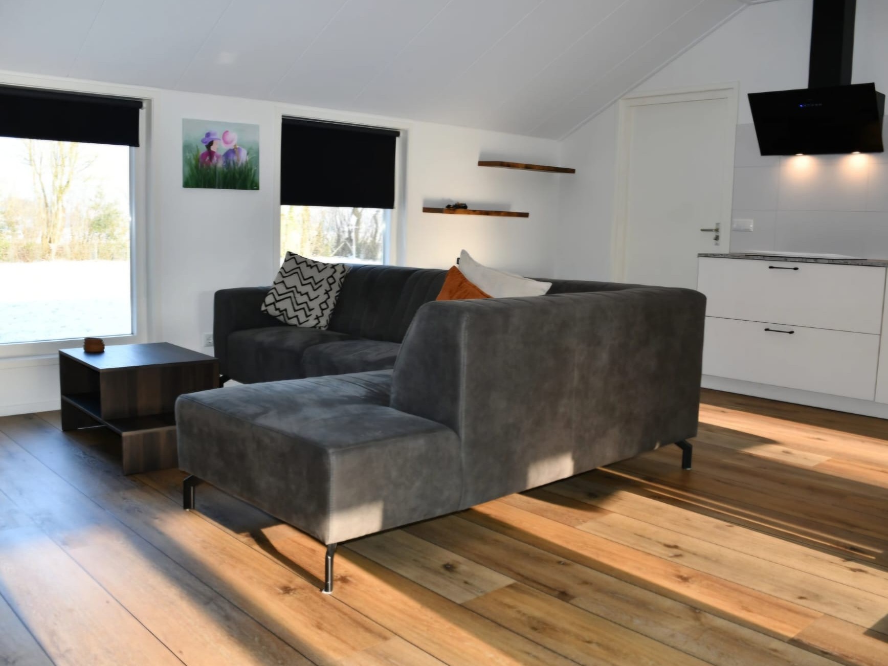 De woonkamer van het luxe zomerhuisje, met een grijze hoekbank, een eiken vloer en een open keuken