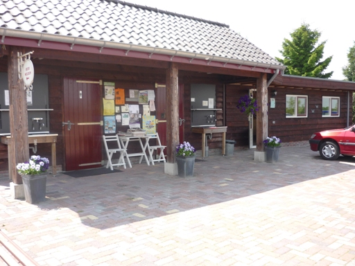 Het houten receptie- en sanitairgebouw met het mededelingenbord