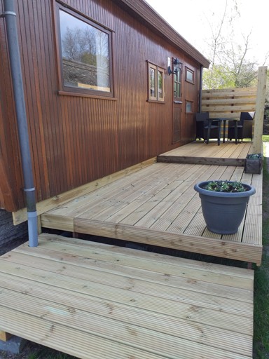 Het houten terras naast de stacaravan, met rieten stoelen en een plantenbak